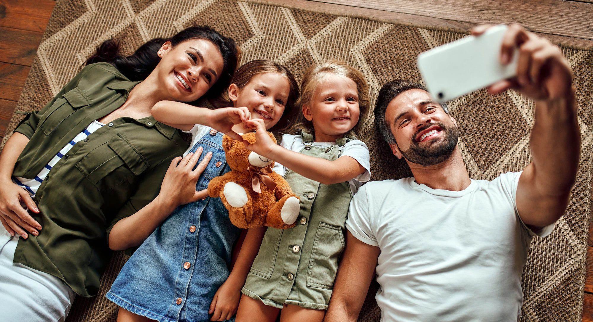 A family laying on the ground with their teddy bear.